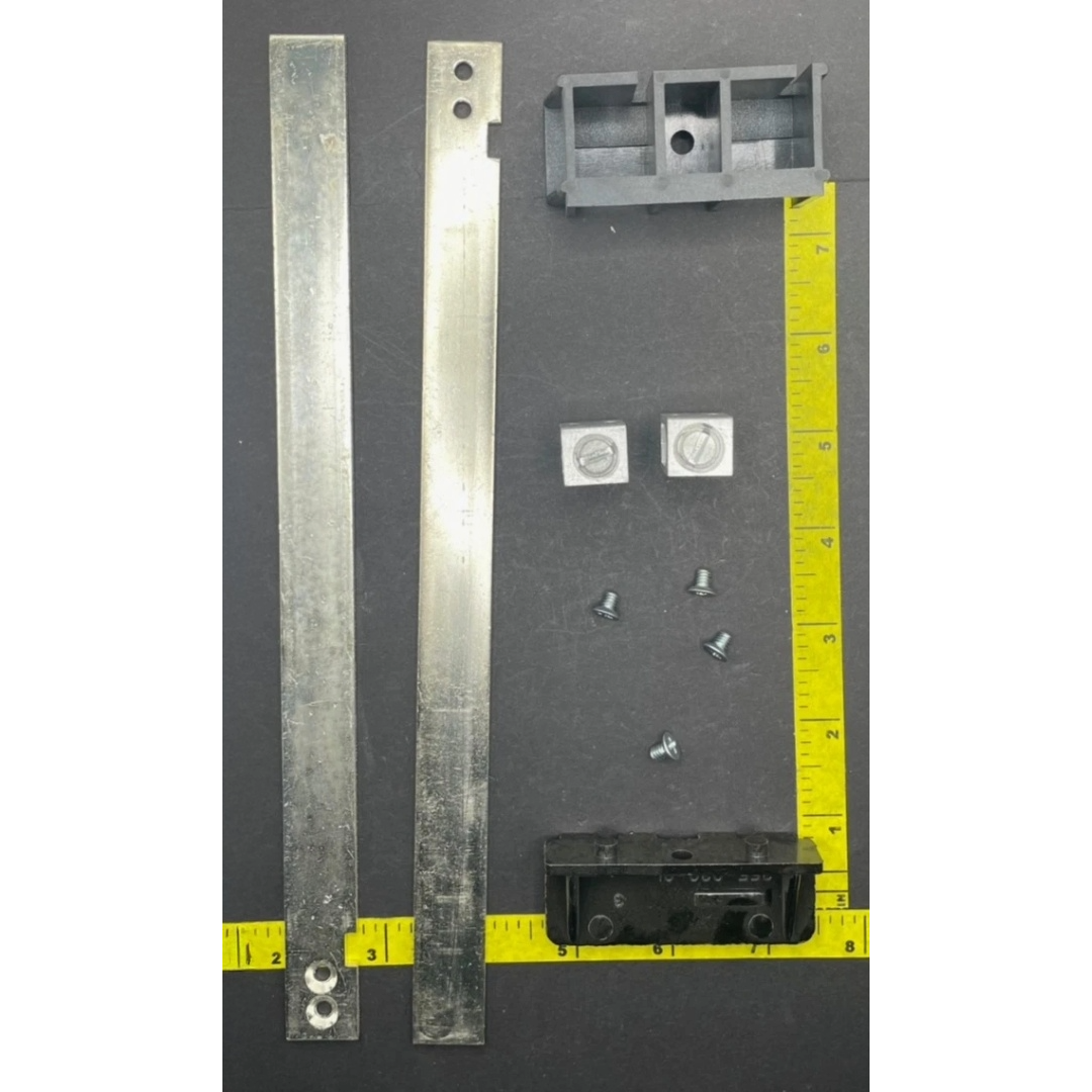 Metal brackets and screws on a gray surface with a tape measure for scale.